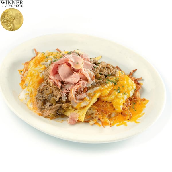 A breakfast skillet with hash browns, melted cheese, pulled pork, and sliced ham on a white plate.